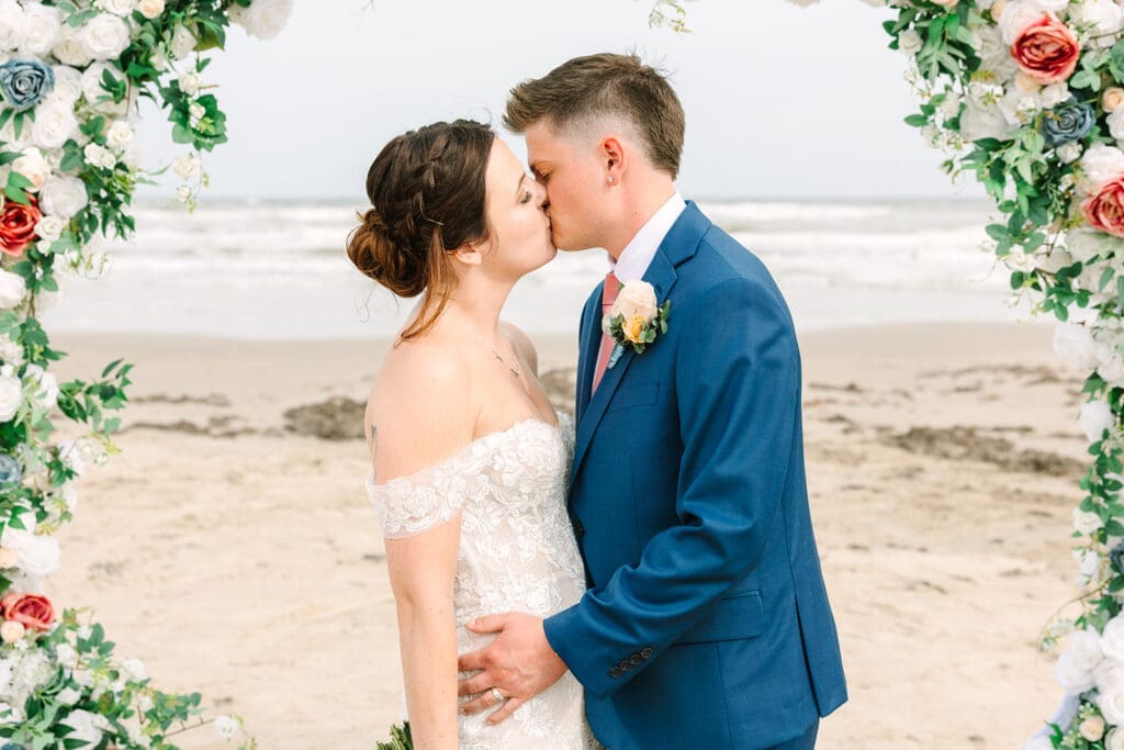 Bride and groom sharing their first kiss during a beachfront wedding ceremony at Stahlman Park in Surfside Beach, Texas.